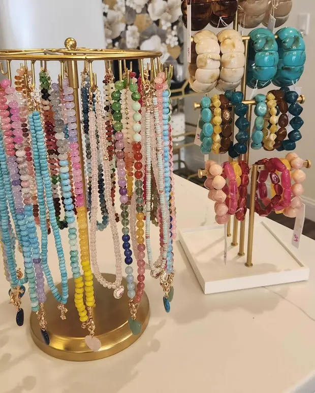 A gold carousel stand hung with beaded necklaces in many colours, beside a tiered stand of chunky stone and resin bracelets.